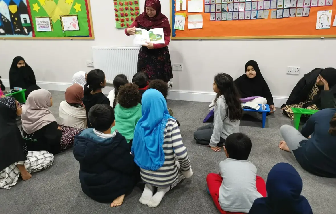 Natalie Mohammed reading Soldier Alif and the Arabic Alphabet to a room full of children sitting on the floor.