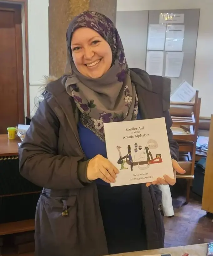Natalie Mohammed holding a copy of Soldier Alif and the Arabic Alphabet at a book stall.